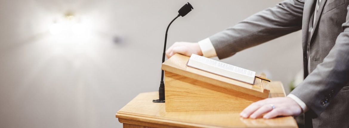 A male in a formal outfit preaching the Holy Bible from the tribune at the altar of the church