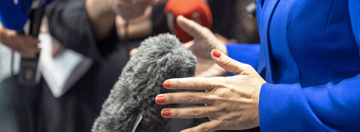 Journalist holding microphones making media interview with female politician or business woman