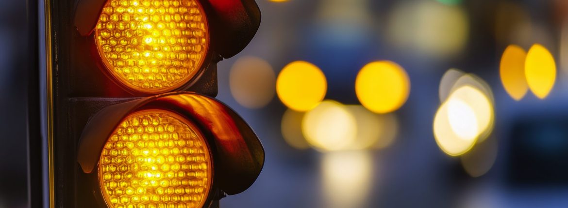 A close-up of a traffic light showing yellow, signaling caution as vehicles approach.